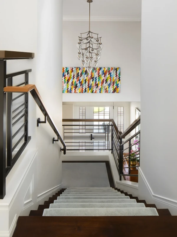 Modern staircase with sleek railings, a colorful wall art, and a stylish chandelier above.