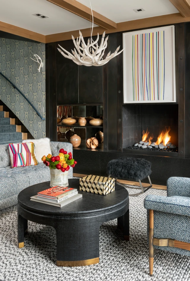 Modern rustic living room with a fireplace, antler chandelier, and colorful decor accents.