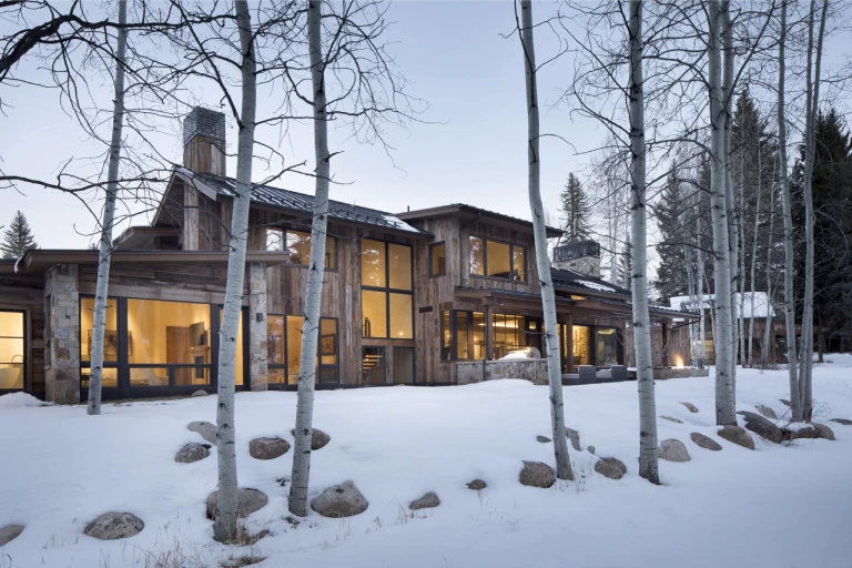 Modern rustic home with big windows, surrounded by snow and trees, with a detached barn & pond view